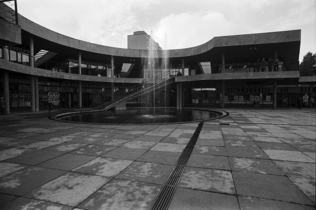 Ostoskeskus Puhoksen viuhkamainen sisäpiha kuvattuna vuonna 1970. Pyöreää pihaa kiertää kaksikerroksinen terassirakenne, jossa liiketiloja. Keskellä sisäpihaa suihkulähde.