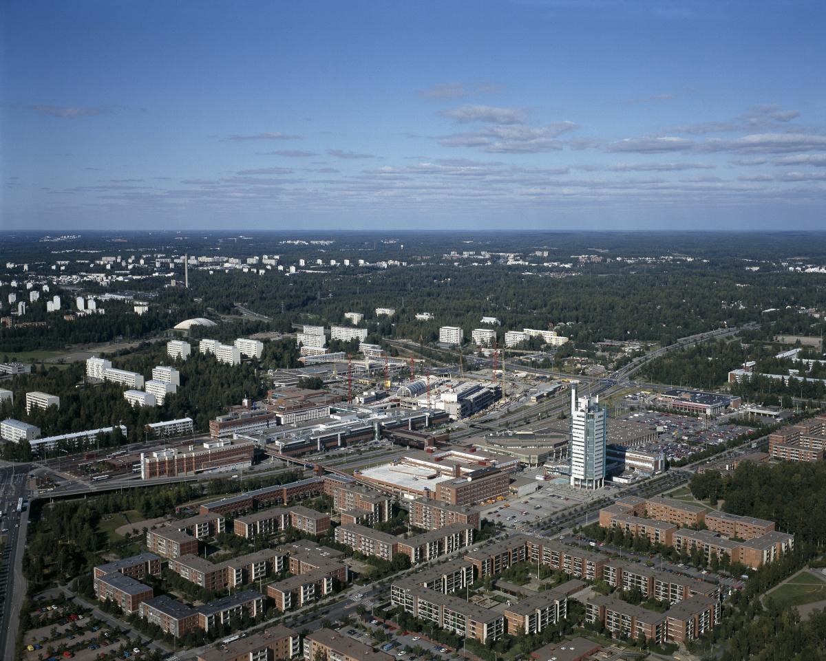 Itäkeskuksen kaupunginosa kuvattuna ilmasta etelästä pohjoiseen. Etualalla Itäväylän eteläpuolella tiivistä asuinrakentamista ja Maamerkki-tornitalo. Itäväylän päällä ostoskeskus, taustalla Puotinharjun vanhempia kerrostaloja ja metsää.
