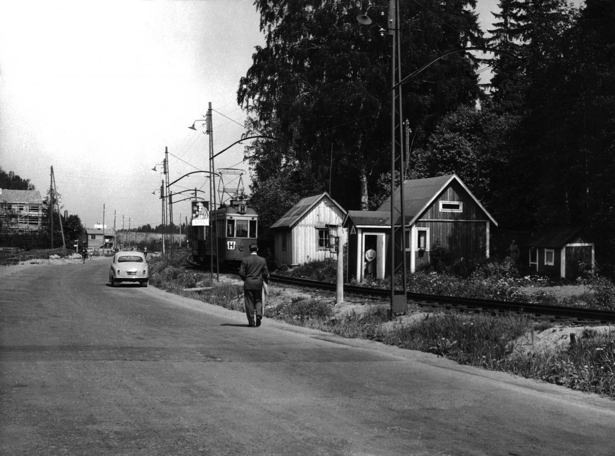 Spårvagn i Stenhagen, på framgrunden väg med en bil och en man som går längs vägen.