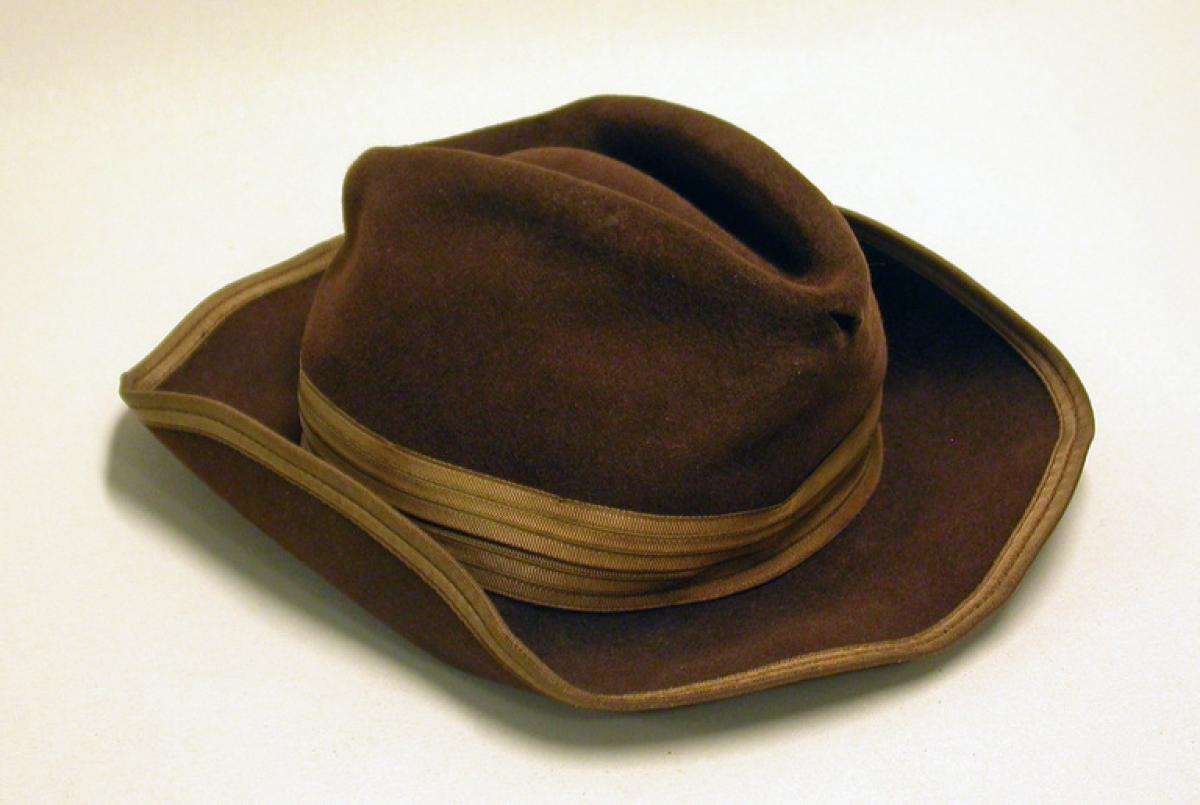 Ruskea ns. lättähattu. Perinteinen miesten hattu, jonka kupu on painettu kasaan ja lieriä on taivuteltu. 