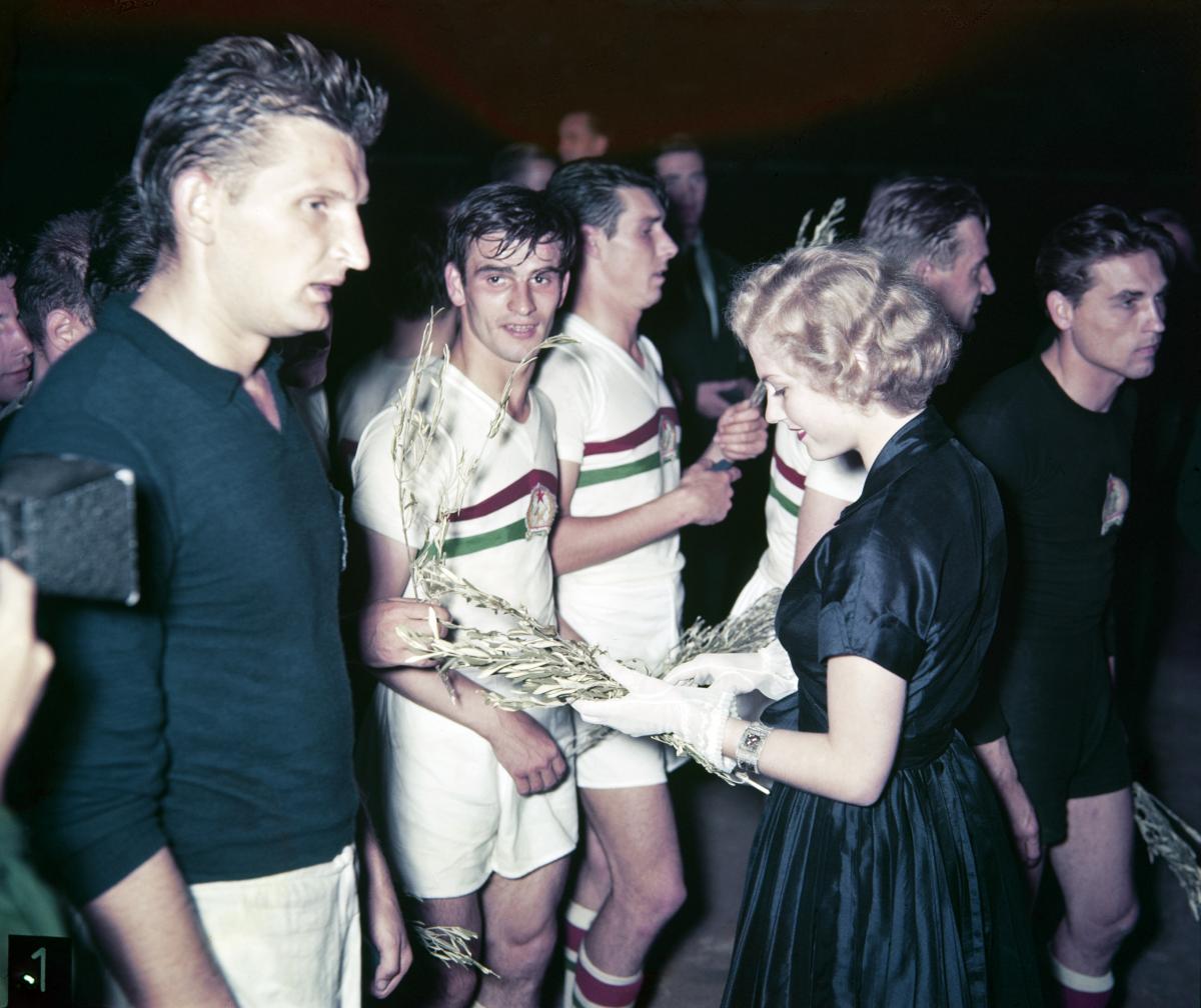A young blond woman giving green branches to young men in shorts