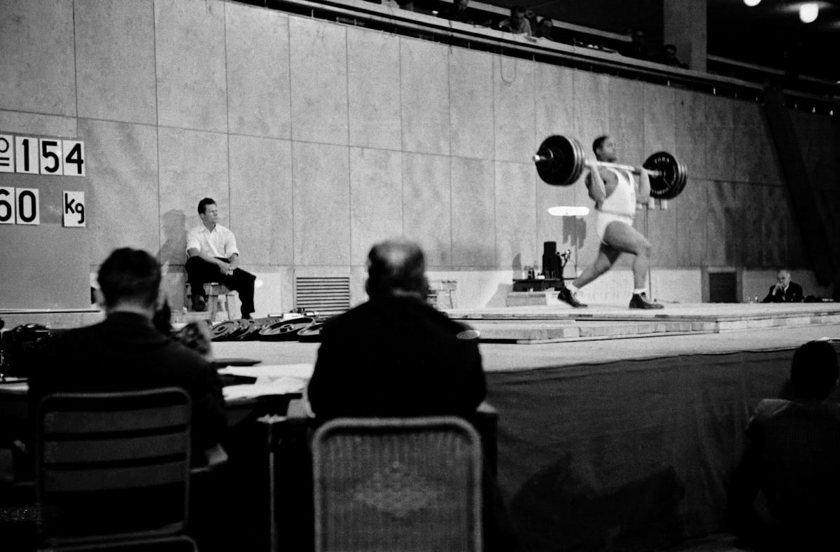 A man lifting heavy weights in a sports hall.