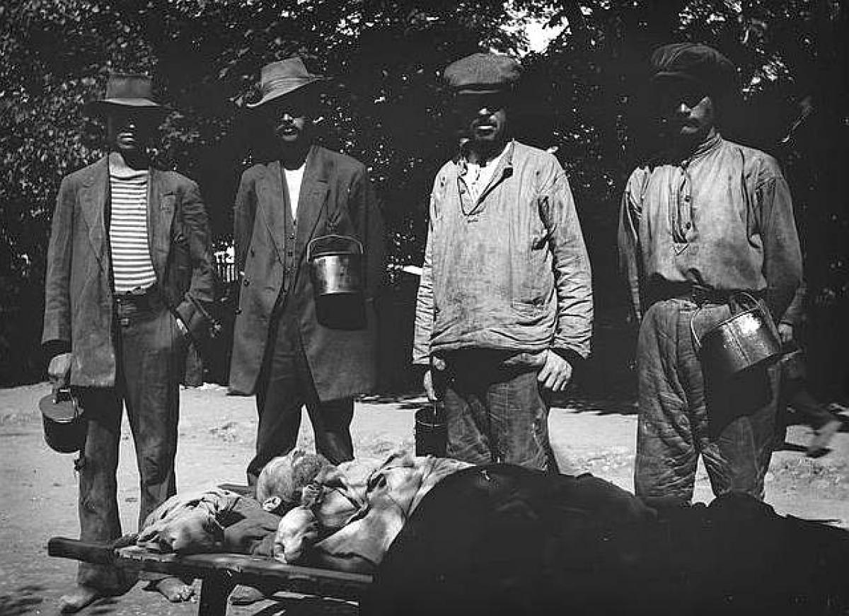 Sisällissodan punavankeja Suomenlinnan vankileirillä. Neljä miestä seisoo maassa paareilla makaavan kuolleen miehen takana.