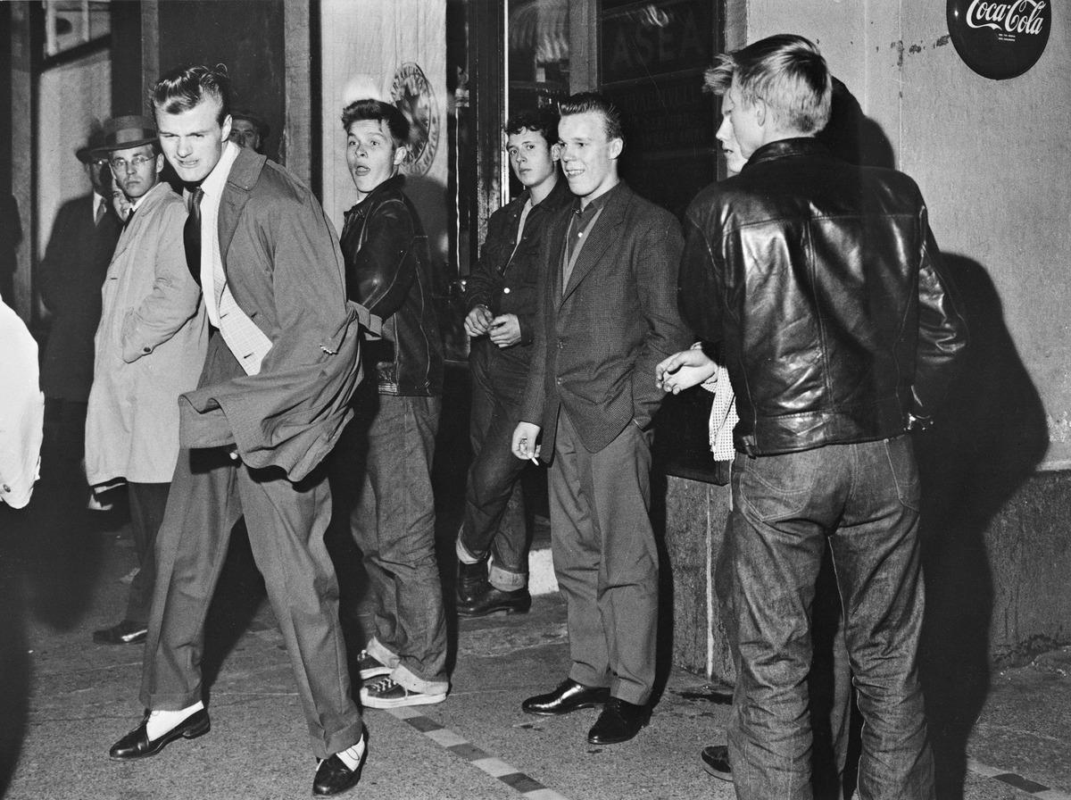 Ungdomar klädda i rock’n’rollstil en kväll i Helsingfors år 1959. Fem unga män bär liknande frisyr och löst sittande herrkostymer eller läderjackor.
