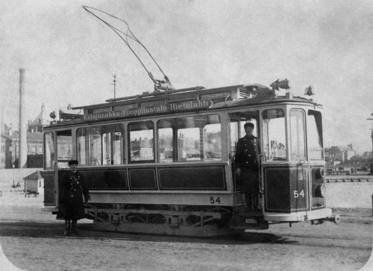 1900-luvun alun sähköraitiovaunu. Ajolanka on ylhäällä, raitiovaunun etuovella seisoo mies.
