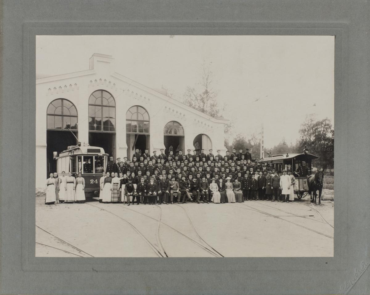 Hevos- ja sähkövetoinen raitiovaunu ja henkilökuntaa asettuneena ryhmäkuvaan vuonna 1900 Töölön hallilla