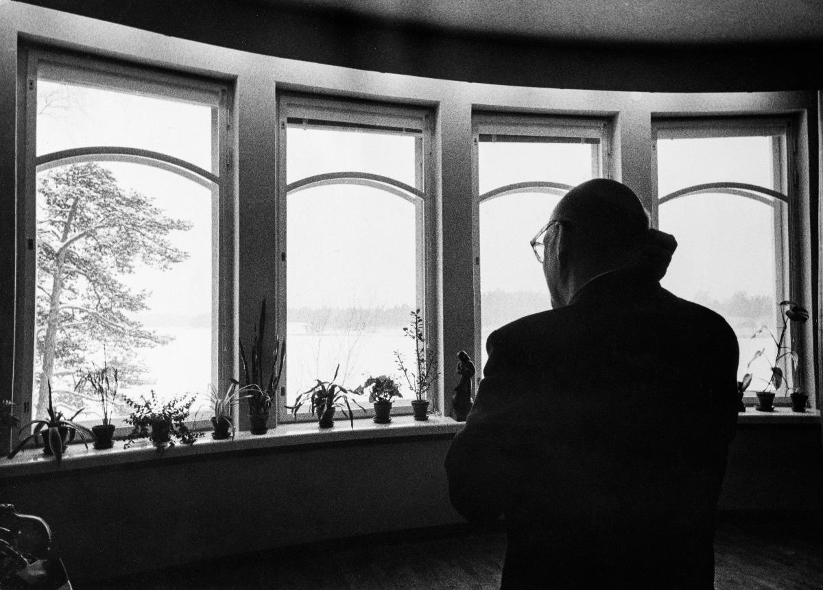 Republikens president Urho Kekkonen förbereder sig för nyårstalet av året 1959 i Ekudden. Han står med ryggen mot fotografen och tittar ut genom fönstret.