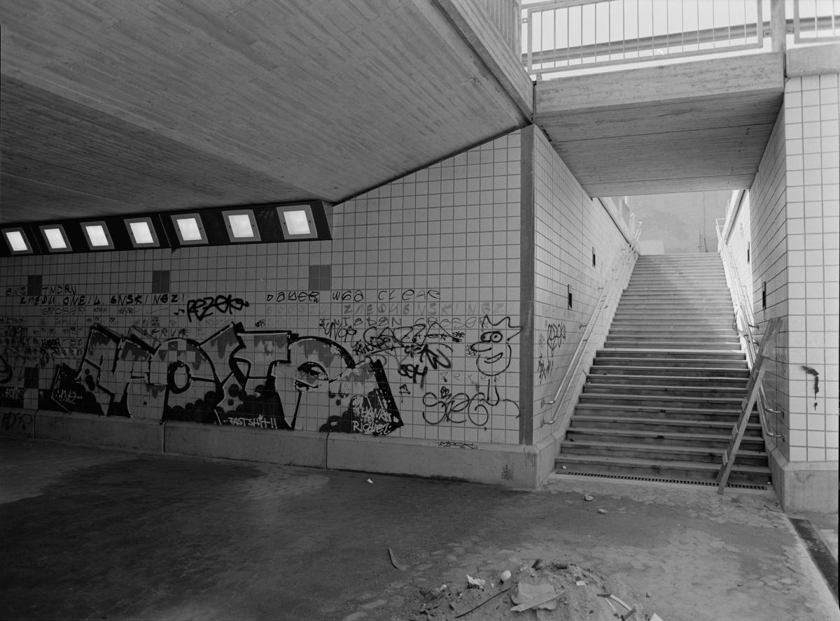 Graffitin i gångtunneln under Porkalagatan. Det svartvita fotografiet visar ett stort antal små tags och en större graffitimålning på tunnelväggen.