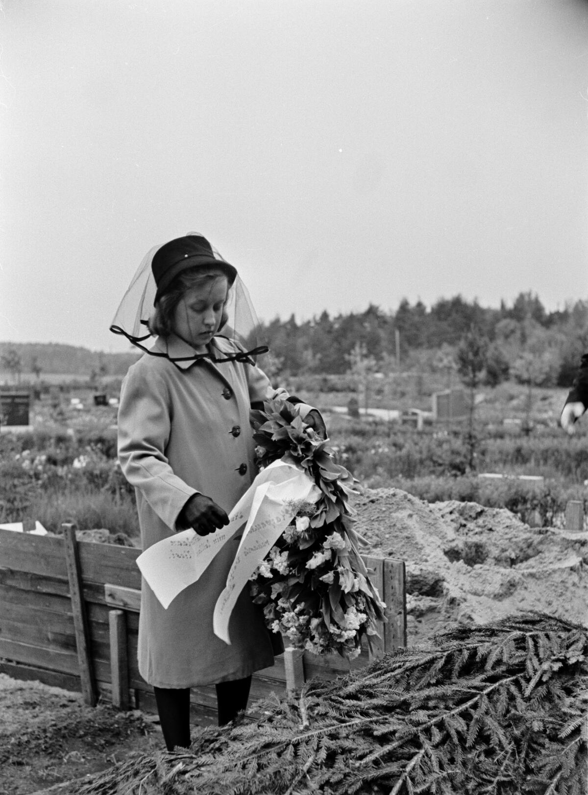 En kvinna i sorgflor lägger en krans på en grav på Norra begravningsplatsen, det vill säga Malms begravningsplats. Foto: Helsingfors stadsmuseum / Väinö Aleksi Kannisto
