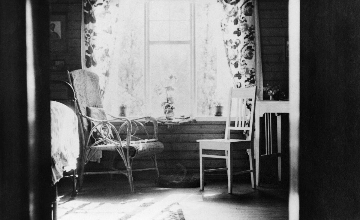 Näkymä huvilan huoneeseen, johon päivänvalo kuultaa sisään ikkunasta. Ikkunan edustalla kaksi tuolia, ikkunassa on kukkakuvioidut verhot.