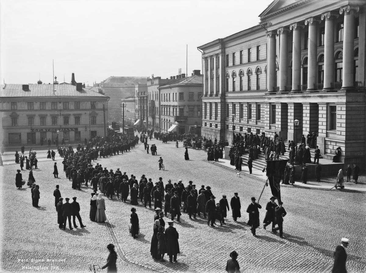Workers' May Day parade on the Senate Square in 1912. In the 1890s, the worker population began celebrating May Day festivities, along with the corresponding marches. The annual May Day march first started to take the form of a protest with the “drinking strike” movement of 1898. In the 20th century, civic addresses, mass meetings, banners, and other symbols became integral May Day markers. The Senate Square became the central destination and often the end point of the marches.  Photo: Helsinki City Museum / Signe Brander 