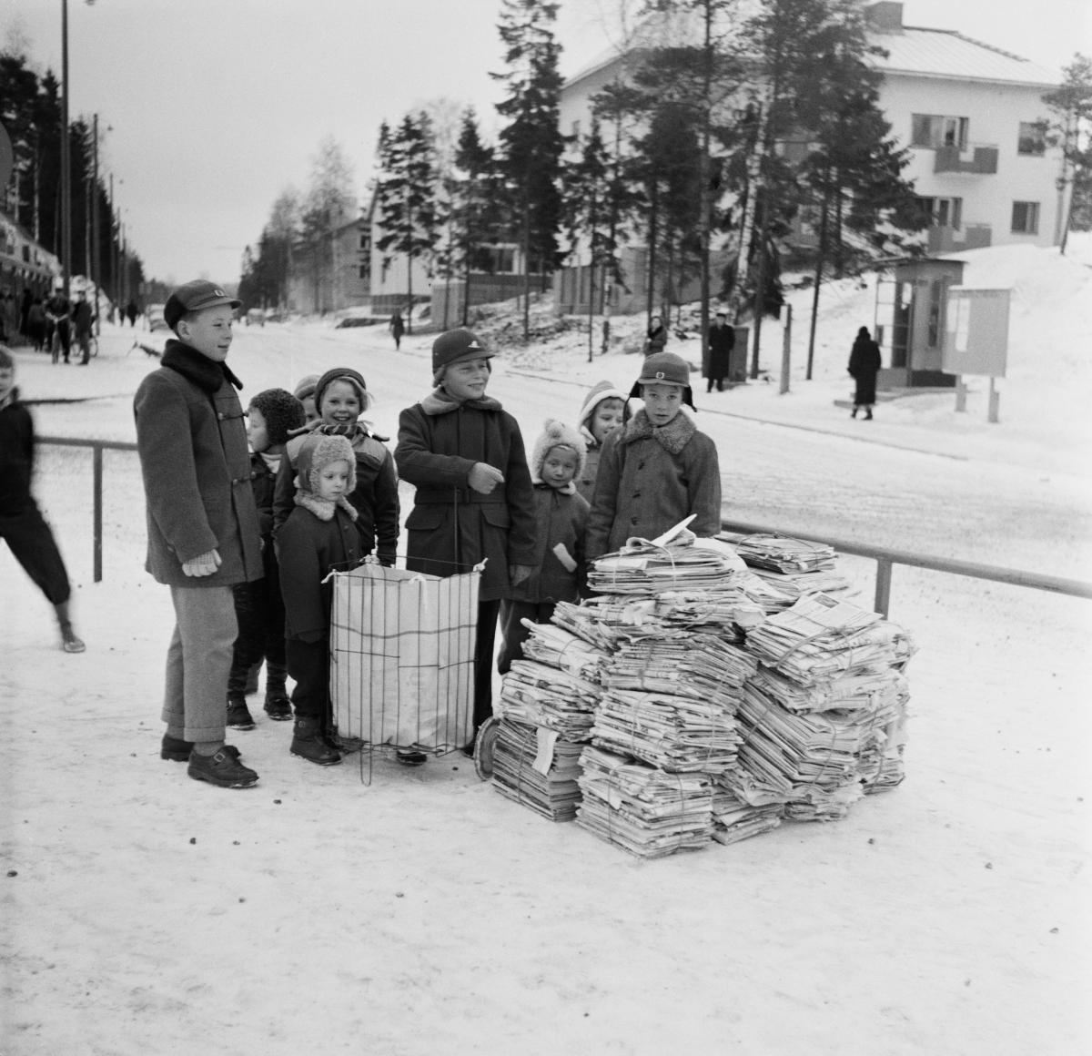 Koululaiset paperinkeräyspinojen kanssa Herttoniemessä Eränkävijäntorilla talvella 1957, HKM.