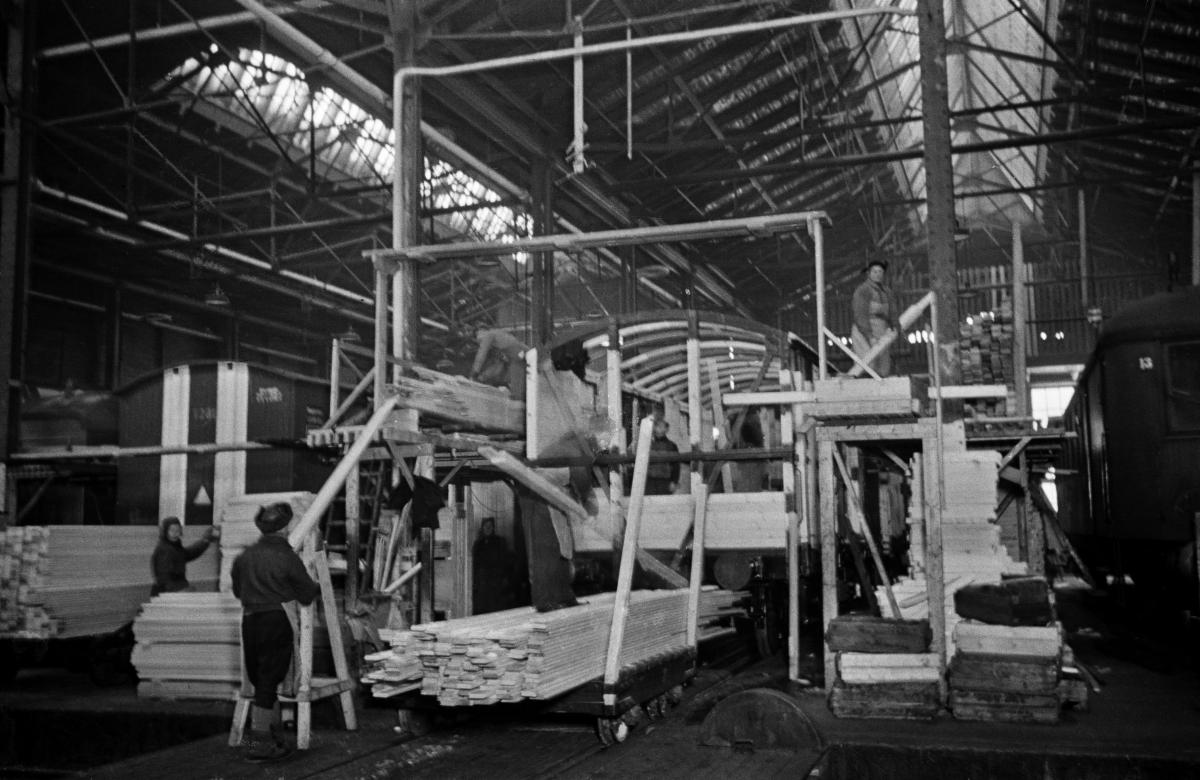 Työntekijöitä rakentamassa junanvaunua VR:n Pasilan konepajan hallissa. Vaunun ympärillä on pinoittain puutavaraa.