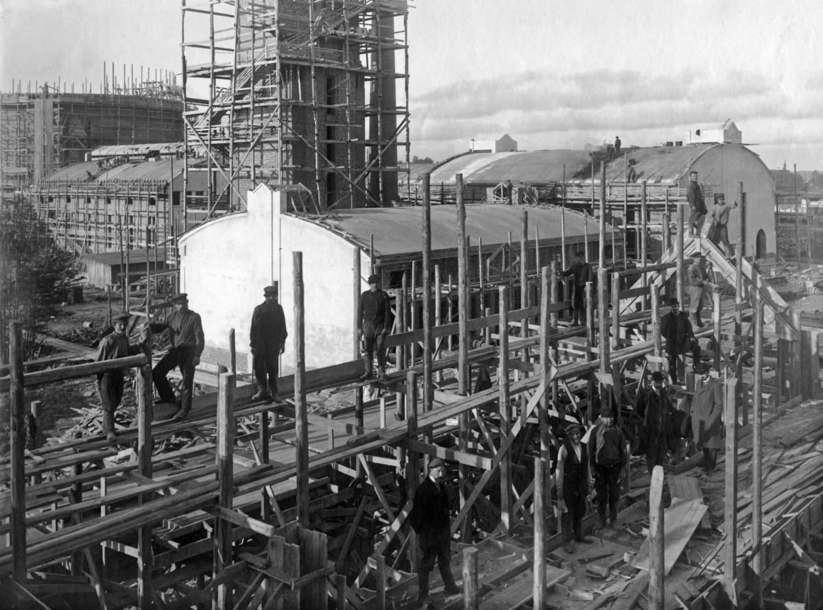 En grupp arbetare står på byggställningar av trä på byggplatsen för Helsingfors stads gasverk i Södervik.