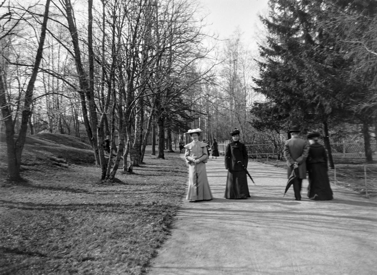 Kaksi tyylikkäästi pukeutunutta vanhempaa naista kävelee kohti kameraa Kaivopuiston puistokadulla. 