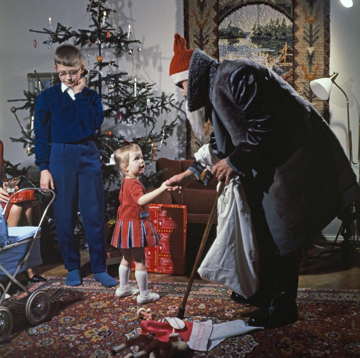 Joulukuusen ohella myös joulupukki on ollut yleinen näky helsinkiläiskodeissa. Tällä 1960-luvun pukilla takki on harmaa ja vain lakki punainen. Aurinkolasit suojaavat kuusen kynttilöiden loisteelta. Juha Jernvall/HKM/Finna.