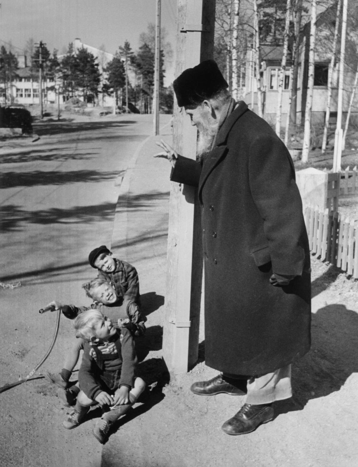 Nobelförfattaren Frans Eemil Sillanpää hälsar på barn på en gata i Hertonäs. Foto E. Heinonen, början av 1950-talet. Foto: Helsingfors stadsmuseum / E. Heinonen