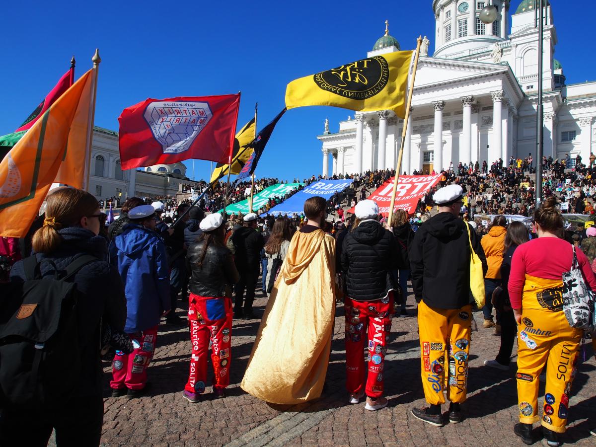 Climate March #2 on 6 April 2019. The marchers gathered at the Senate square prepare to head towards the Parliament building. In the foreground, representatives of student organisations dressed in overalls carry the flags of their organisations.  Photo: Helsinki City Museum / Anette Helander