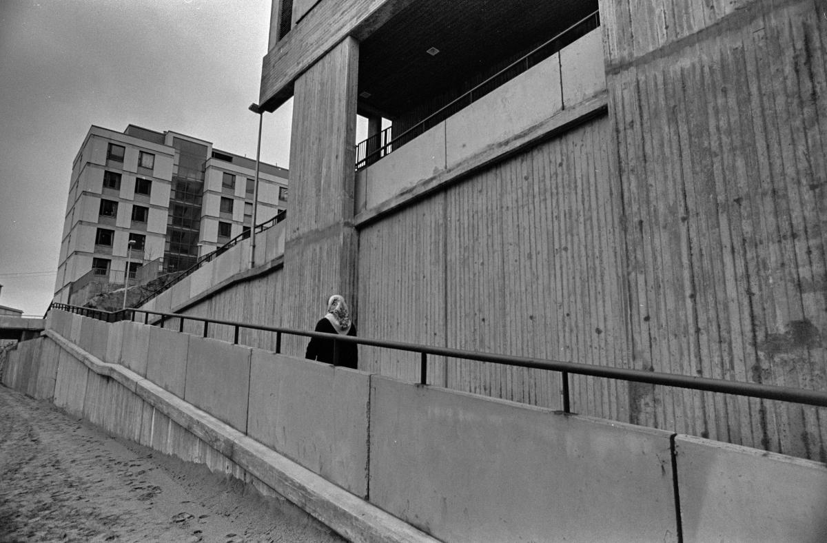 En kvinna går på den gångramp som leder till Dressingränden i Östra Böle. I bakgrunden reser sig ett stort betongelementhus. 