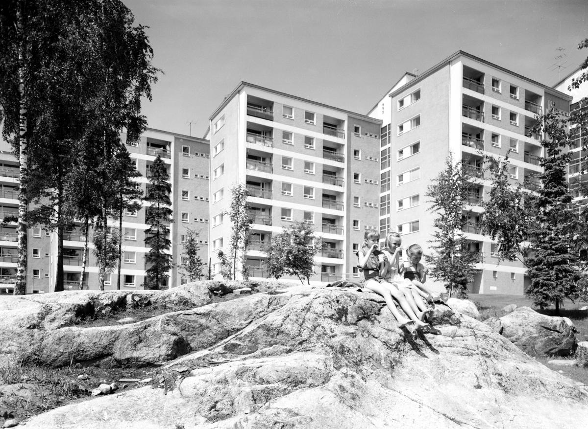 Uusia, vieri viereen rakennettuja 7-kerroksisia asuintaloja Herttoniemessä 1950-luvulla. Etualalla kaksi lasta istuu kalliolla.
