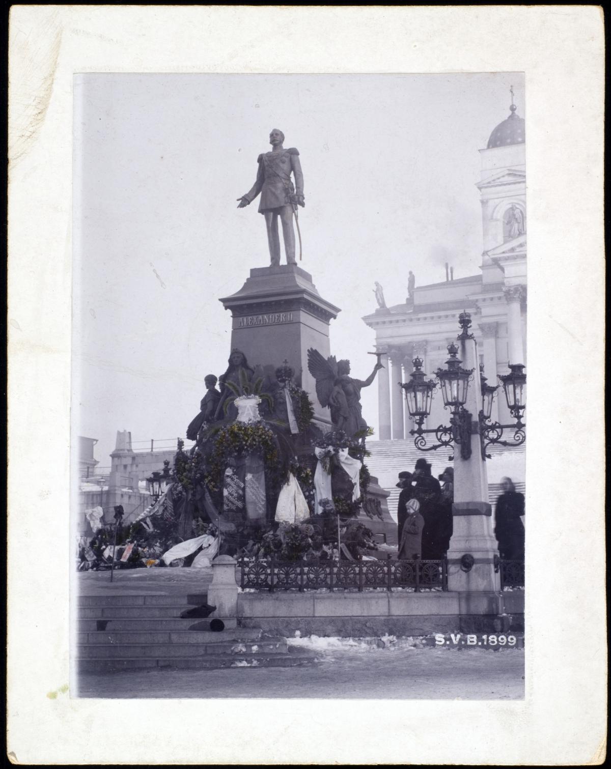 Blommor har med anledning av det ovälkomna Februarimanifestet lagts ned vid kejsar Alexander II:s staty den 13 mars 1899 (på årsdagen av hans död). Foto: Signe Brander / Helsingin kaupunginmuseo