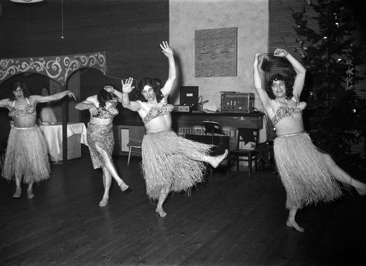 Miehet tanssivat pukeutuneina havaijilaistyylisiin naisten asuihin, todennäköisesti Elannon pikkujoulujuhlissa. Kuvaaja: Helsingin kaupunginmuseo