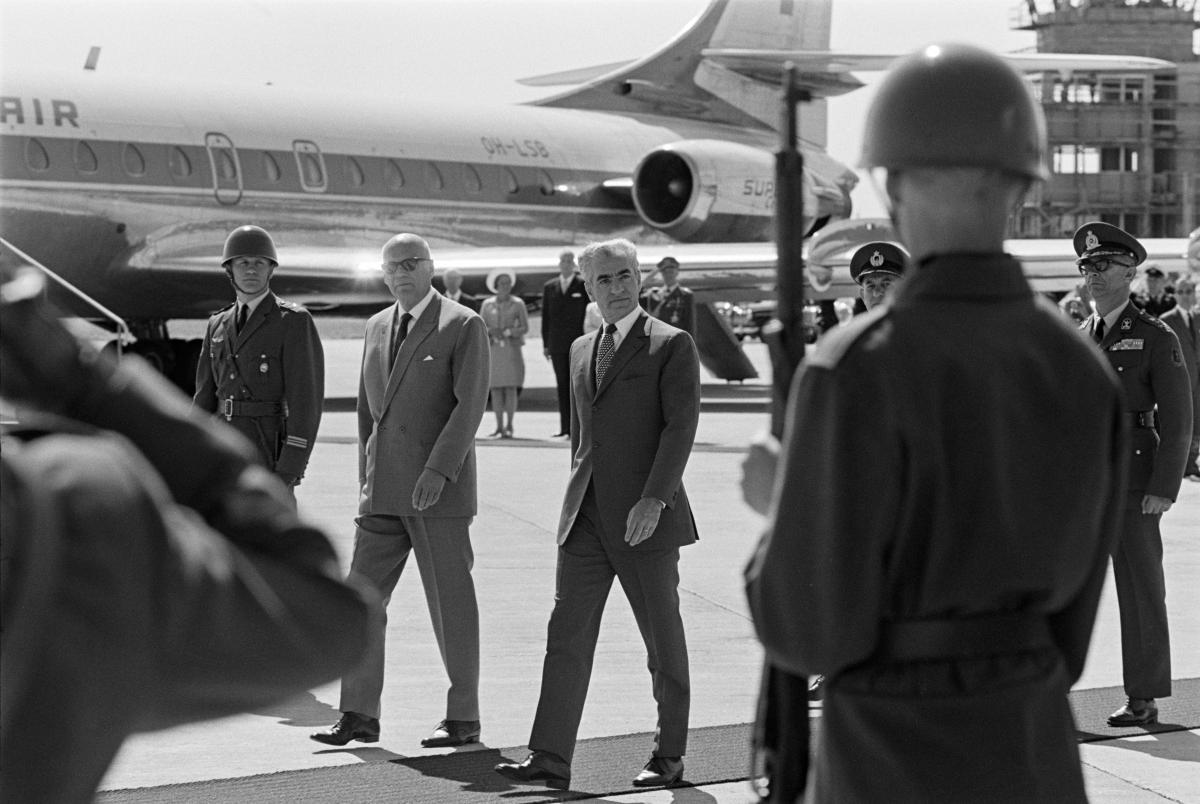 Presidentti Kekkonen ja Iranin shaahi Seutulan lentokentällä poliisien ja sotilaiden ympäröiminä. Heidän takanaan on lentokone.