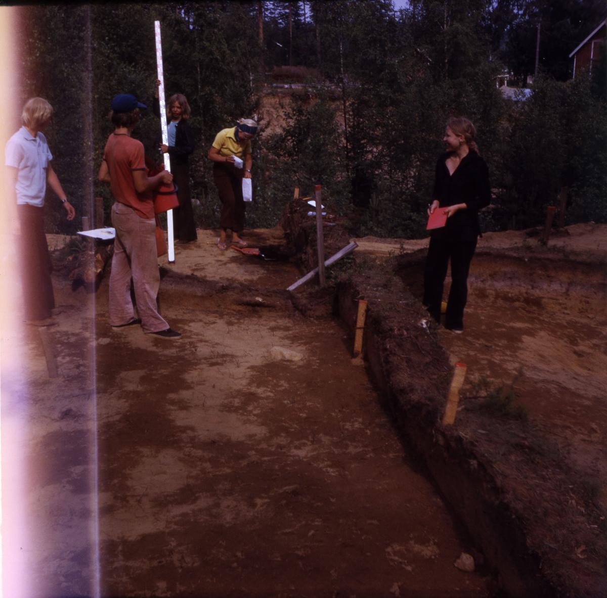 Ryhmä arkeologeja seisoo arkeologisen kaivannon ympärillä.